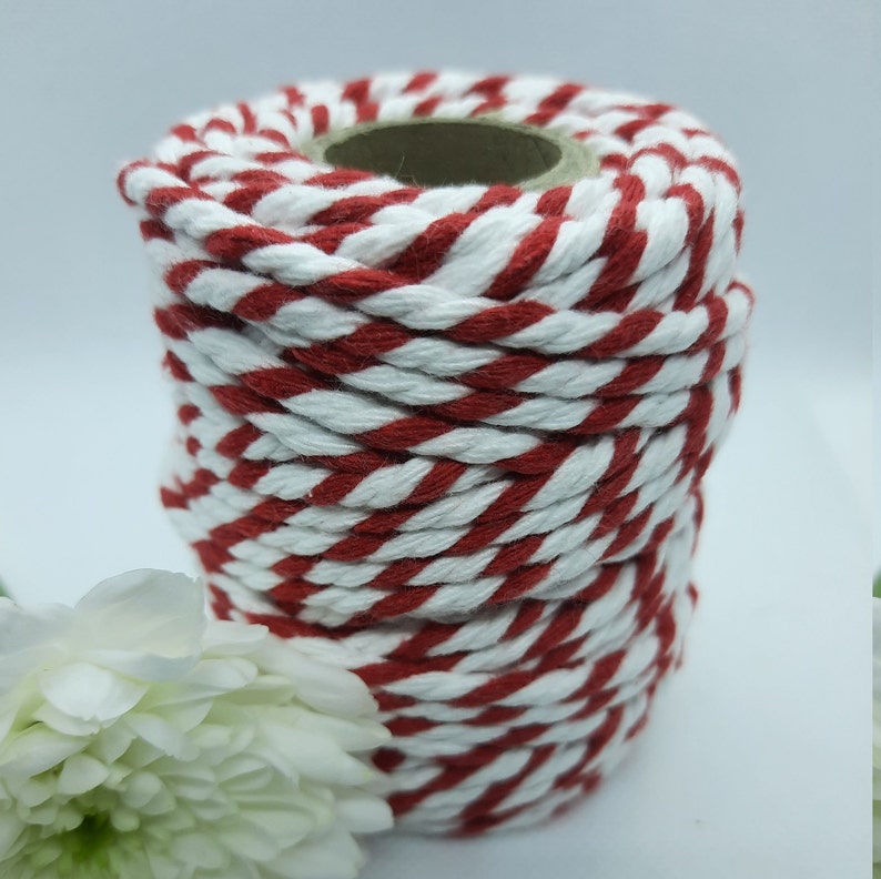 May include: A spool of red and white striped twine. The twine is tightly wound around a cardboard core. The colors are a vibrant red and clean white, creating a classic, festive look. The twine is suitable for crafts and gift wrapping.
