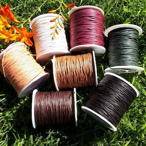 May include: Spools of waxed cotton cord in a variety of colours, including white, brown, red, black and green. The spools are arranged on a bed of green grass.