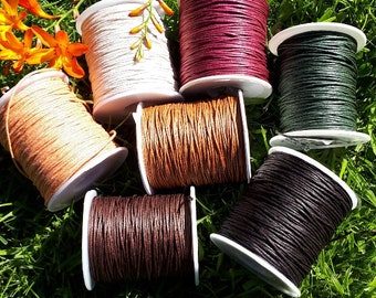 May include: Spools of waxed cotton cord in various colors, including white, brown, red, black, and green. The spools are arranged on a bed of green grass.