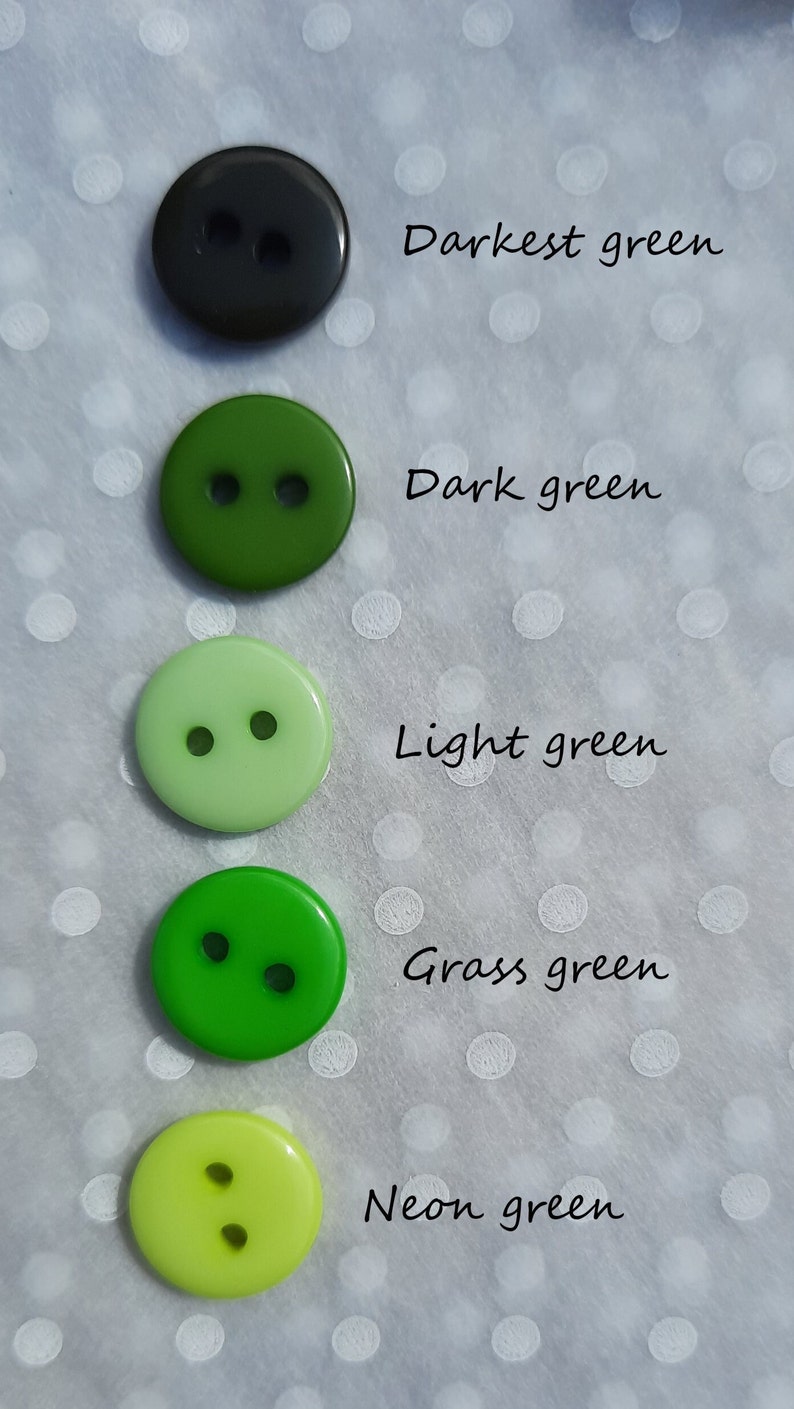 May include: Five round plastic buttons in various shades of green, from darkest green to neon green. Each button has two holes.