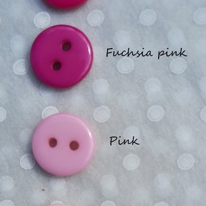 May include: Four plastic buttons in different shades of pink, from hot pink to light pink. The buttons are arranged vertically, with the darkest shade at the top and the lightest shade at the bottom. Each button has two holes.