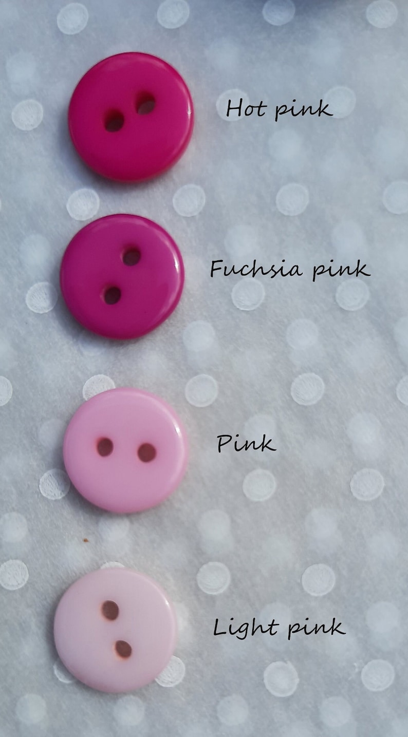 May include: Four plastic buttons in different shades of pink, from hot pink to light pink. The buttons are arranged vertically, with the darkest shade at the top and the lightest shade at the bottom. Each button has two holes.