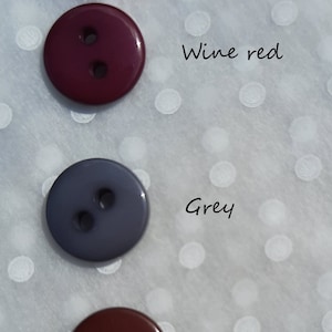 May include: Four round buttons in different colors: red, wine red, gray, and coffee. The buttons are arranged vertically on a white background with white polka dots.
