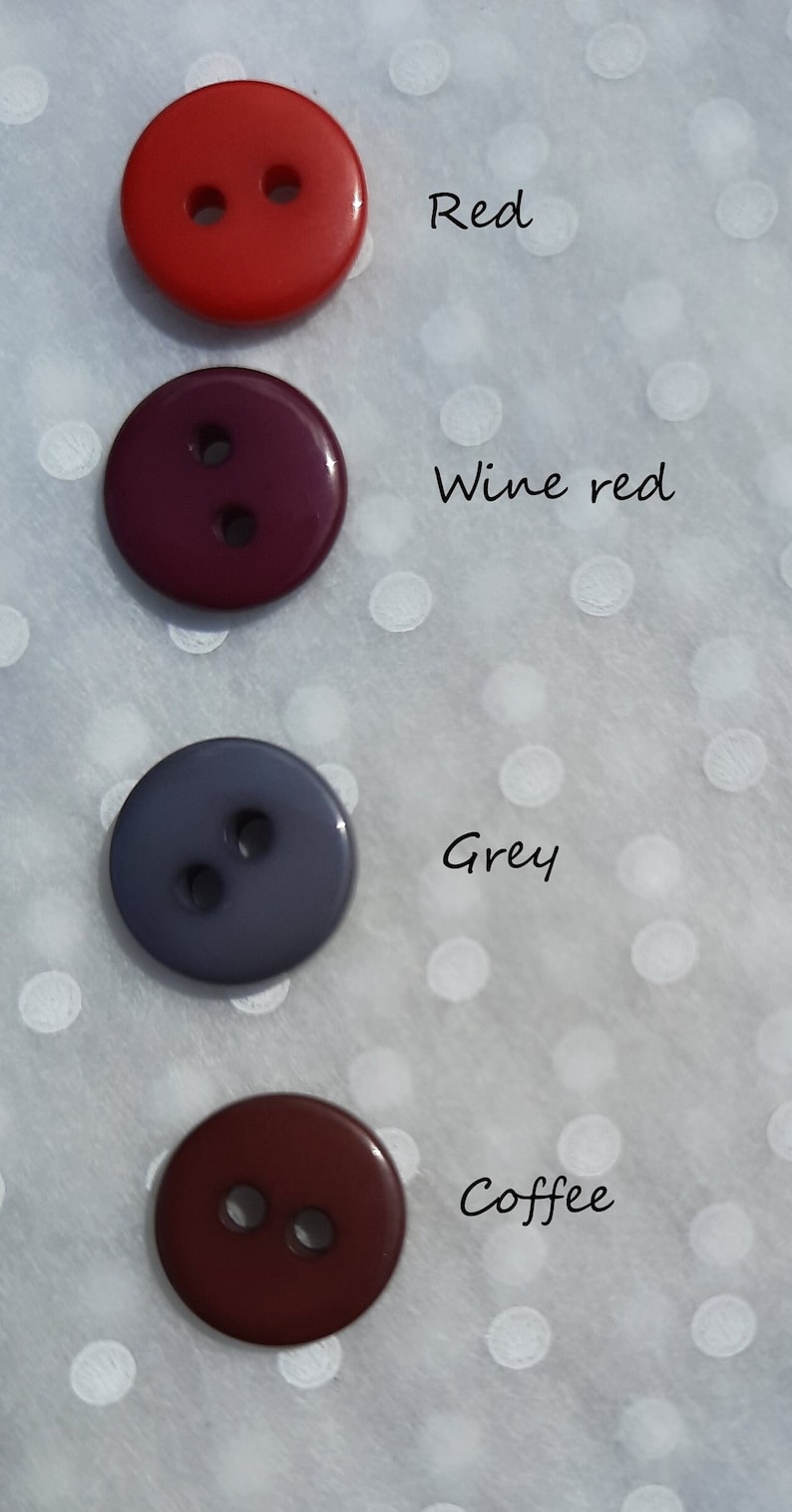 May include: Four round buttons in different colors: red, wine red, gray, and coffee. The buttons are arranged vertically on a white background with white polka dots.