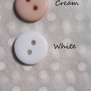 May include: Two buttons, one cream and one white, with two holes each. The buttons are on a white background with white polka dots.