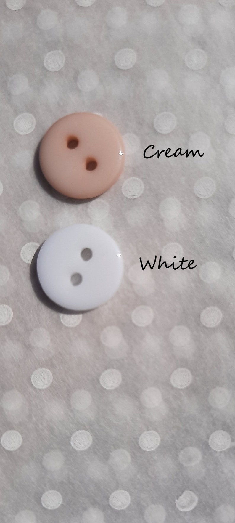 May include: Two buttons, one cream and one white, with two holes each. The buttons are on a white background with white polka dots.