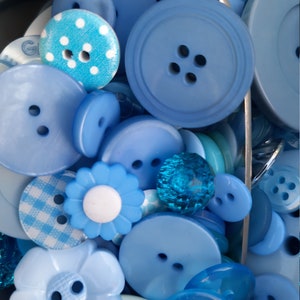 May include: A collection of various blue buttons in different shapes and sizes. Some buttons are solid, others have patterns like polka dots and gingham. There are also flower-shaped and faceted buttons. The buttons vary in shades of blue, from light to dark.