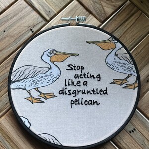 May include: Embroidered hoop art with two white pelicans and the text "Stop acting like a disgruntled pelican".