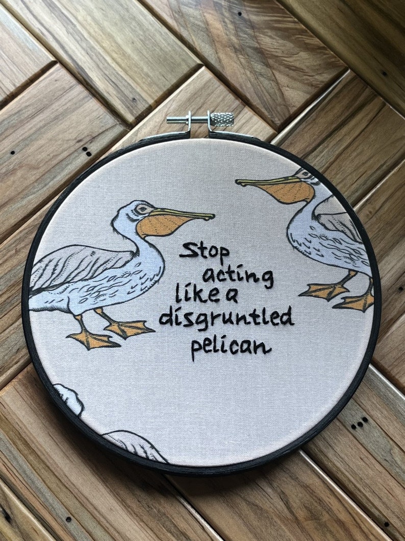 May include: Embroidered hoop art with two white pelicans and the text "Stop acting like a disgruntled pelican".