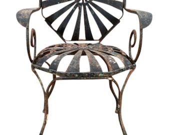 May include: A rusty metal garden chair with a sunburst design on the back and seat. The chair has a curved back and arms, and the legs are slightly curved.