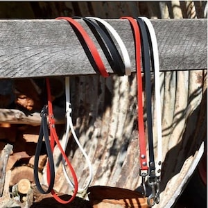 May include: A collection of dog leashes in red, black, and white, hanging from a wooden beam. The leashes are made of a smooth material and feature silver-colored metal clasps.