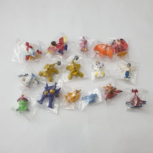 May include: A collection of 15 small plastic figurines in individual clear plastic bags. The figurines are various colors, including red, blue, green, yellow, and white. They depict different characters from the Digimon anime series.