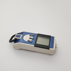 May include: A blue, white, and black Digimon digital pet toy. The handheld device features a small screen, three gray buttons, and the word "Digimon" printed on the front. A black loop is attached to the top.