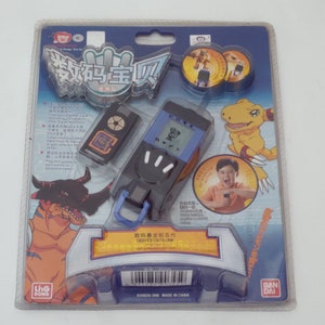 May include: A blue and black Digimon toy with a blue strap and a silver chain. The toy has a screen and buttons. The packaging is blue and features a Digimon character. The text on the packaging reads "Digimon Data Link".