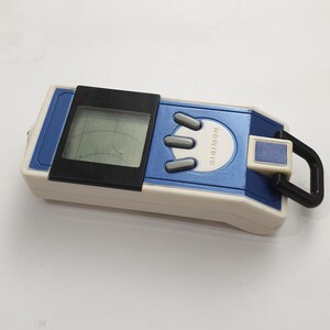 May include: A blue and white Digimon digital pet toy with a black screen and three gray buttons. The toy has a black carabiner clip and the word "DIGIMON" is printed on the blue section.
