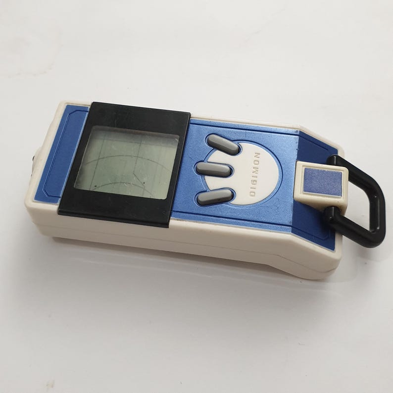 May include: A blue and white Digimon digital pet toy with a black screen and three gray buttons. The toy has a black carabiner clip and the word "DIGIMON" is printed on the blue section.