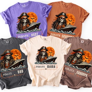 May include: Five short-sleeve t-shirts in purple, orange, dark gray, cream, and brown. Each features a graphic of a skeleton pirate on a cruise ship with a large orange moon, bats, and text reading Pirate Aunt, Grandma, Dad, Mama, and Grandpa.