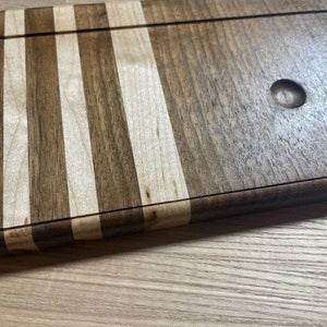 Pu&ograve; includere: Un tagliere in legno con un design a strisce. Il tagliere &egrave; fatto di due tipi di legno diversi, uno chiaro e uno scuro. Il tagliere ha un piccolo foro al centro.