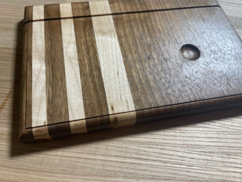 Pu&ograve; includere: Un tagliere in legno con un design a strisce. Il tagliere &egrave; fatto di due tipi di legno diversi, uno chiaro e uno scuro. Il tagliere ha un piccolo foro al centro.