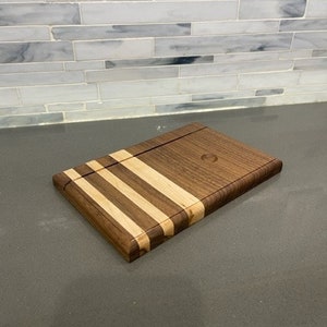 Pu&ograve; includere: Un tagliere in legno con un design in noce e acero. Il tagliere ha una finitura in legno naturale ed &egrave; perfetto per servire formaggio, salumi o altri antipasti.