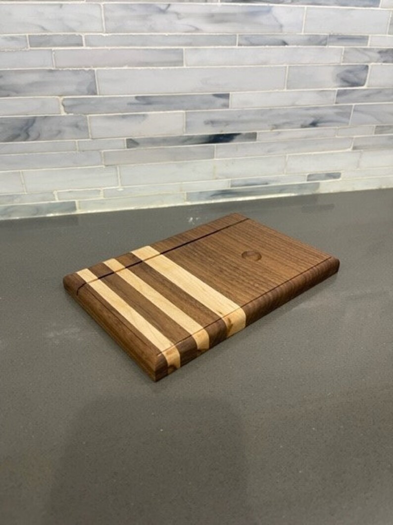 Pu&ograve; includere: Un tagliere in legno con un design in noce e acero. Il tagliere ha una finitura in legno naturale ed &egrave; perfetto per servire formaggio, salumi o altri antipasti.