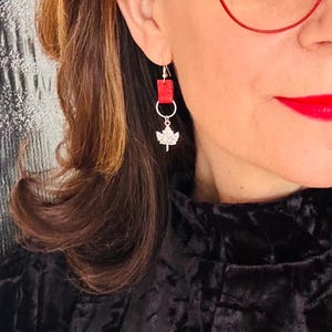 May include: Silver maple leaf dangle earrings with a red leather accent.