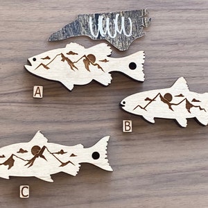 May include: Three wooden fish ornaments with a mountain and sun design. The fish are labeled A, B, and C.