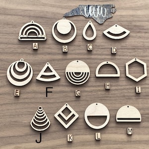 May include: A set of 13 wooden earring shapes, including a rainbow, a circle with a crescent moon, a teardrop, a half-circle, a circle with concentric circles, a triangle with concentric circles, a circle with concentric circles, a half-circle, a hexagon, a cone with concentric circles, a square with concentric squares, a circle with a half-circle, and a half-circle.