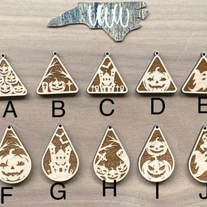 May include: Ten wooden Halloween-themed ornaments in the shape of triangles and teardrops. The ornaments feature various designs, including pumpkins, ghosts, and a haunted house.
