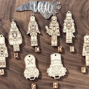 May include: Eight wooden nutcracker ornaments with different designs. The ornaments are unfinished and ready to be painted. The ornaments are labelled with letters A through H.