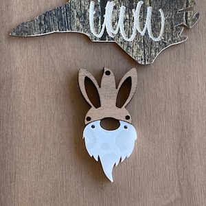 May include: A wooden bunny rabbit ornament with a white beard. The bunny has a brown wooden body and white beard with a dotted pattern.
