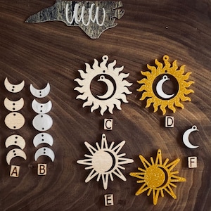 May include: Wooden celestial-themed ornaments and cutouts, including sun and moon designs, and a North Carolina state cutout with the word "WWW". The ornaments are in various colors and finishes, perfect for crafting or decor.