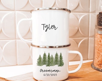 Puede incluir: Taza de camping de esmalte blanco con borde plateado. La taza tiene un diseño de acuarela verde de pinos y el texto "Groomsman 6/10/2023". El nombre "Tyler" está escrito en la parte superior de la taza.