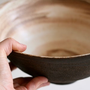May include: A large, brown ceramic bowl with a white interior. The bowl has a rough, textured exterior and a smooth, glazed interior.