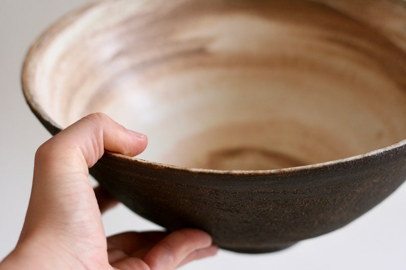 May include: A large, brown ceramic bowl with a white interior. The bowl has a rough, textured exterior and a smooth, glazed interior.