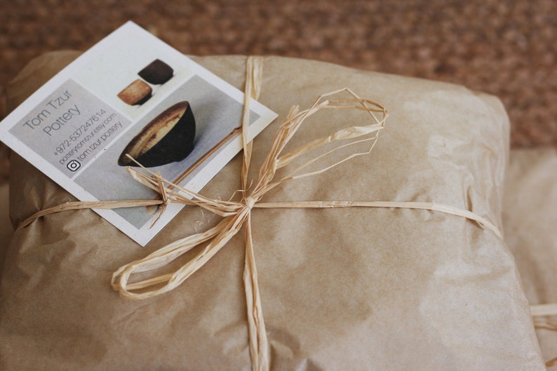 May include: A brown paper package tied with a natural twine bow. A business card with the text "Tom Tzu Pottery" and contact information is on top of the package.
