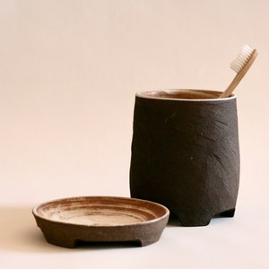 May include: A dark brown ceramic toothbrush holder with a matching lid and a white toothbrush sticking out of the top.