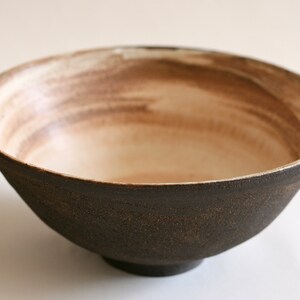 May include: A brown ceramic bowl with a white interior and a subtle brown glaze. The bowl has a wide rim and a rounded base.