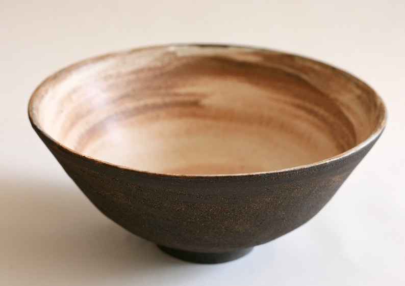 May include: A brown ceramic bowl with a white interior and a subtle brown glaze. The bowl has a wide rim and a rounded base.