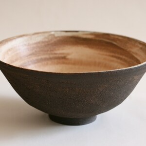 May include: A large, dark brown ceramic bowl with a white interior. The bowl has a slightly flared rim and a rounded base. The interior of the bowl has a subtle brown glaze.