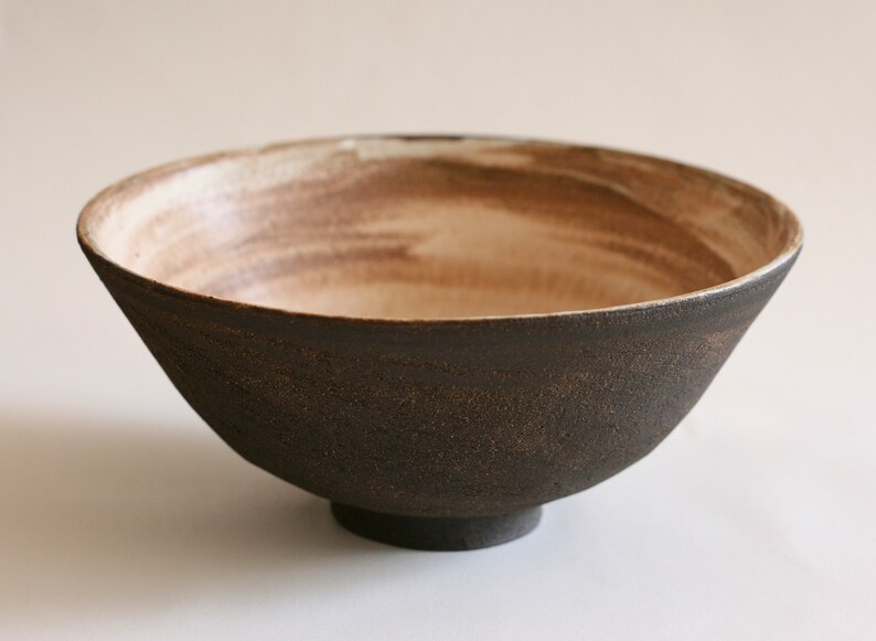 May include: A large, dark brown ceramic bowl with a white interior. The bowl has a slightly flared rim and a rounded base. The interior of the bowl has a subtle brown glaze.