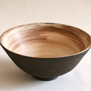 May include: A large, dark brown ceramic bowl with a white interior. The bowl has a subtle, hand-painted design in brown on the inside.