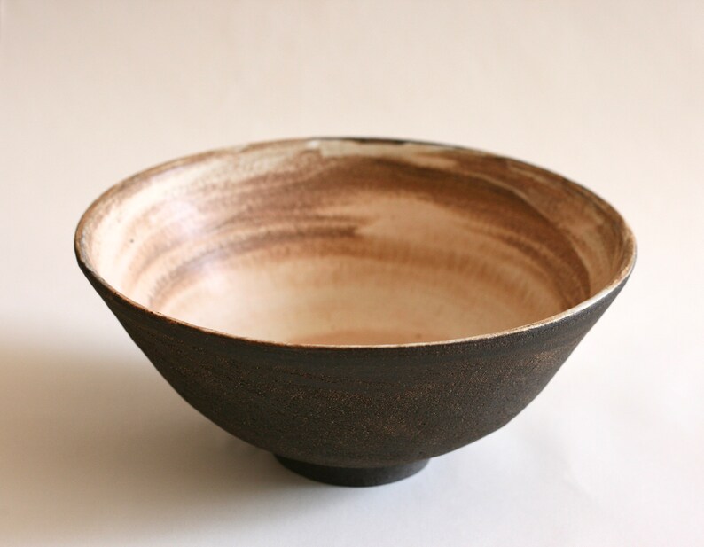 May include: A large, dark brown ceramic bowl with a white interior. The bowl has a subtle, hand-painted design in brown on the inside.