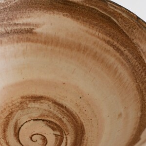May include: A large, white ceramic bowl with a brown glaze. The glaze has a swirling pattern, creating a unique and rustic look.