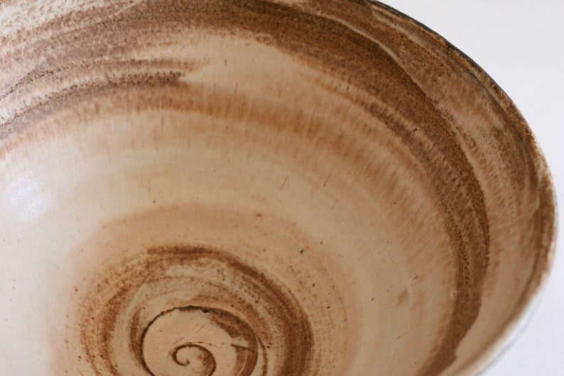 May include: A large, white ceramic bowl with a brown glaze. The glaze has a swirling pattern, creating a unique and rustic look.