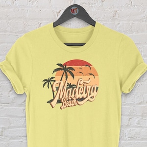 Puede incluir: Camiseta amarilla con un gráfico retro de palmeras y una puesta de sol con el texto "Madeira Beach".