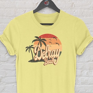 May include: Yellow t-shirt with a retro-style graphic of palm trees and a sunset with the text "Delray Beach".