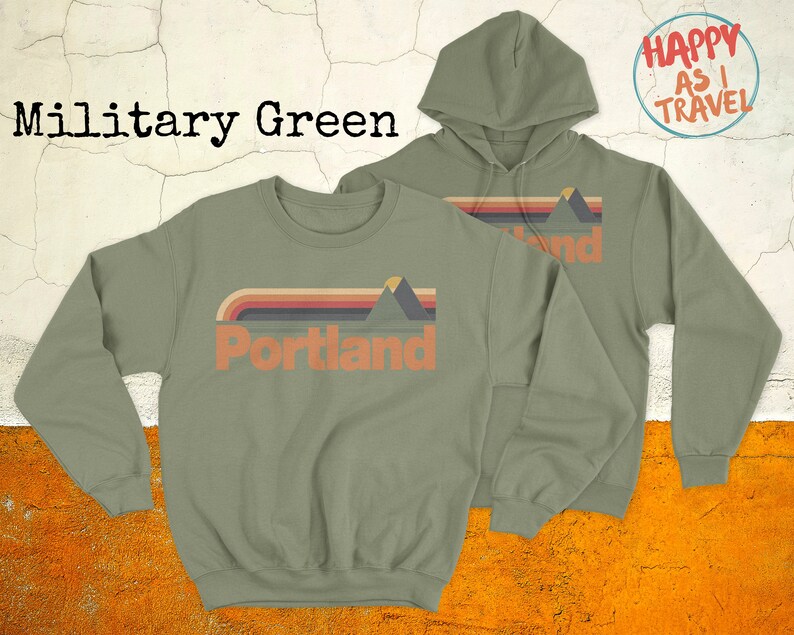May include: Two sweatshirts in military green, one a crew neck and the other a hoodie, both featuring a retro-style graphic of mountains and the word "Portland". The hoodie has the text "Happy as I Travel" on the back.