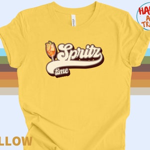 May include: Yellow t-shirt with a retro-style graphic of a glass of Spritz and the text "Spritz time".