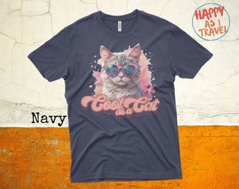 May include: Navy blue t-shirt featuring a cat wearing sunglasses with a pink watercolor background and the text "Cool as a Cat" in a retro font.